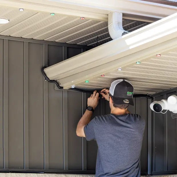Electrician installing gemstone lights along the eaves of a gray home.