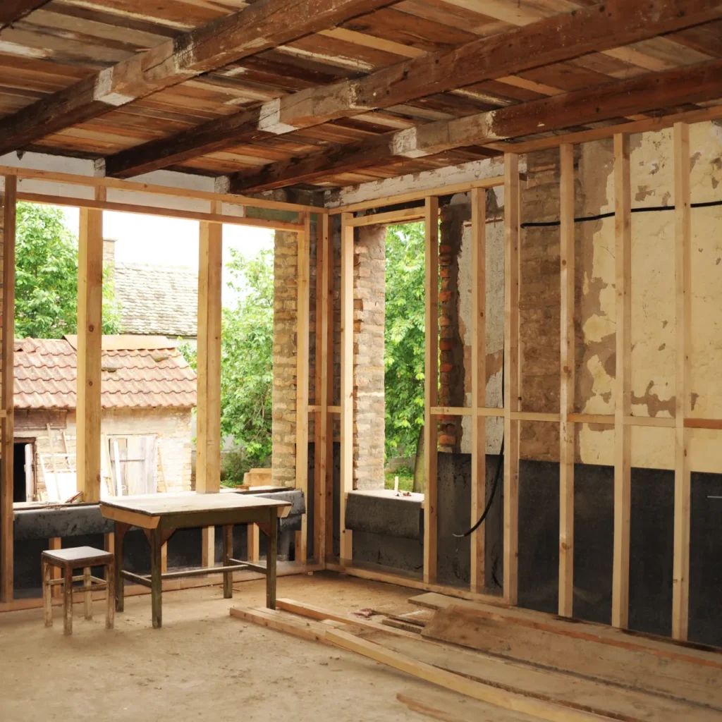 A home addition under construction, with unfinished flooring, studs in place of walls, and exposed wood ceiling.