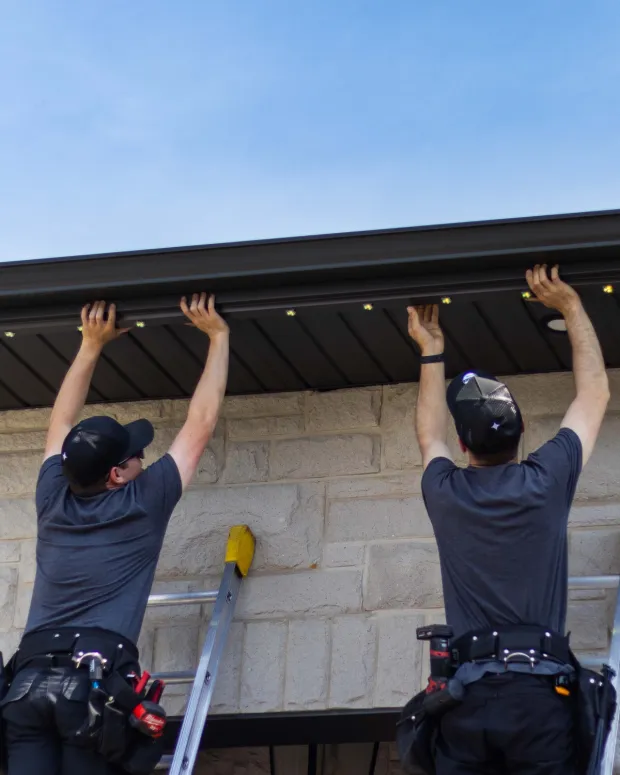 Two installers putting gemstones lights on a home